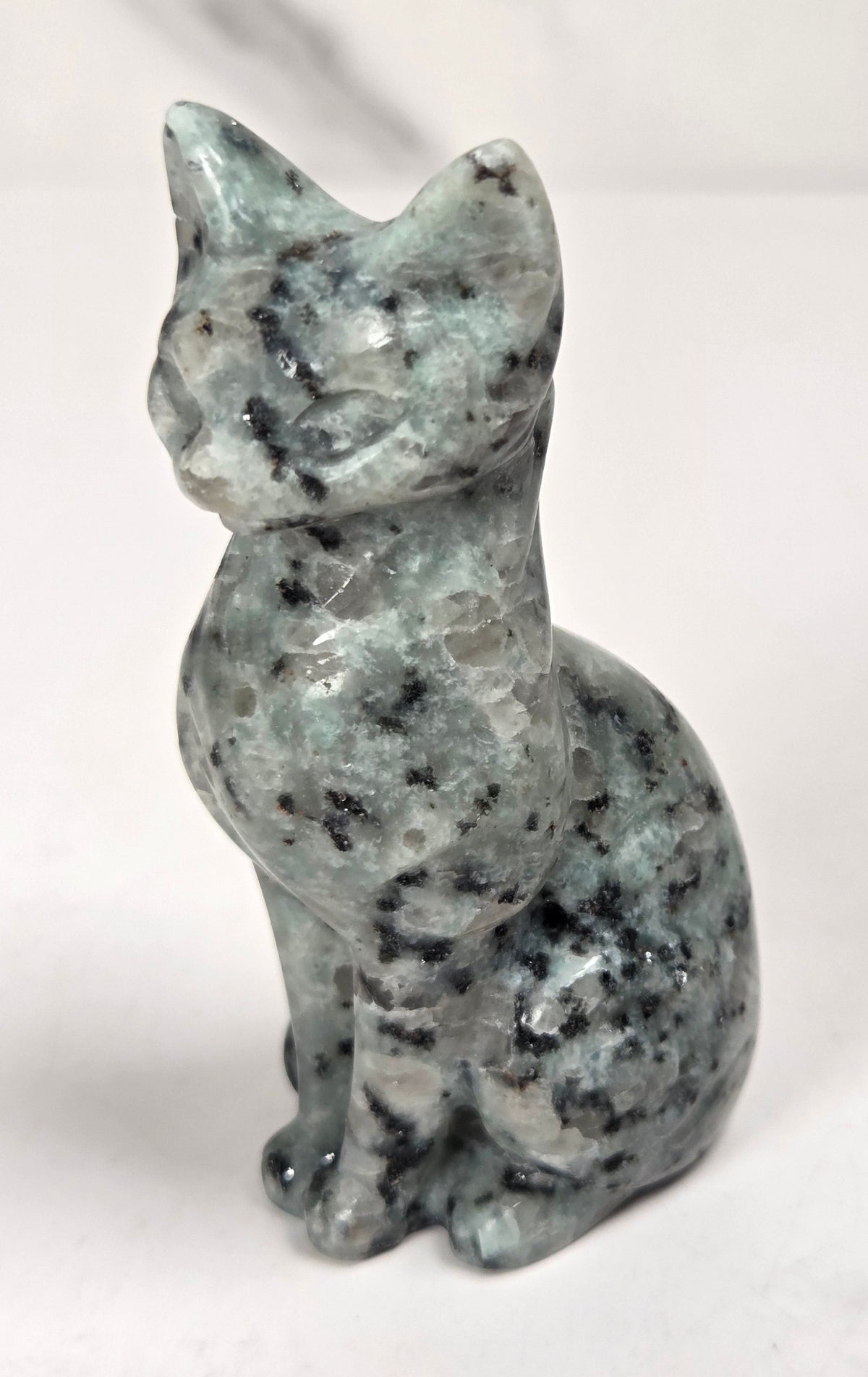 Blue and black spotted crystal cat shaped carving with scroll work against a white background