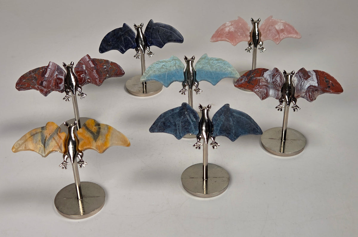 Crystal carved bat wings, in varying colors and materials, on silver stands against a white background