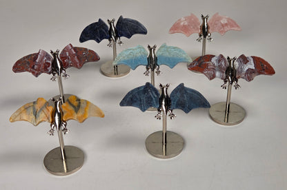 Crystal carved bat wings, in varying colors and materials, on silver stands against a white background