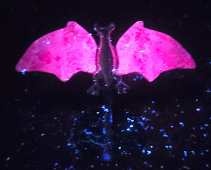 Pink crystal bat wings glowing under a UV light on a silver stand against a white background