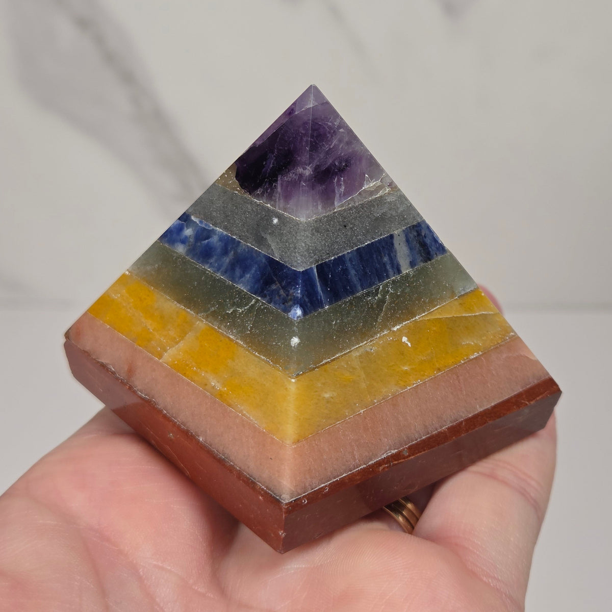 Hand holding a rainbow colored  crystal pyramid carving on a white background