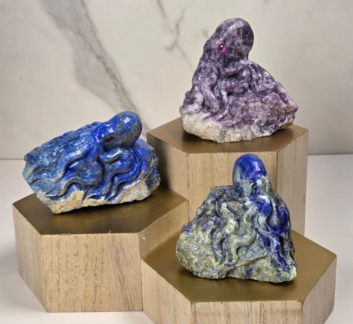 Crystal octopus carvings with different colors and eyes on a wooden stand against a marbled background