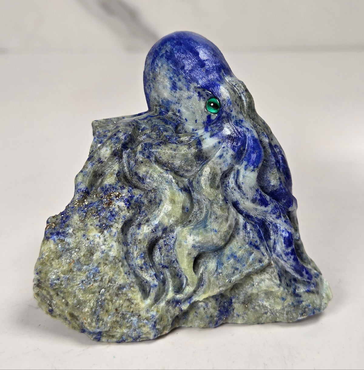Blue crystal octopus carving with green  eyes against a marbled background