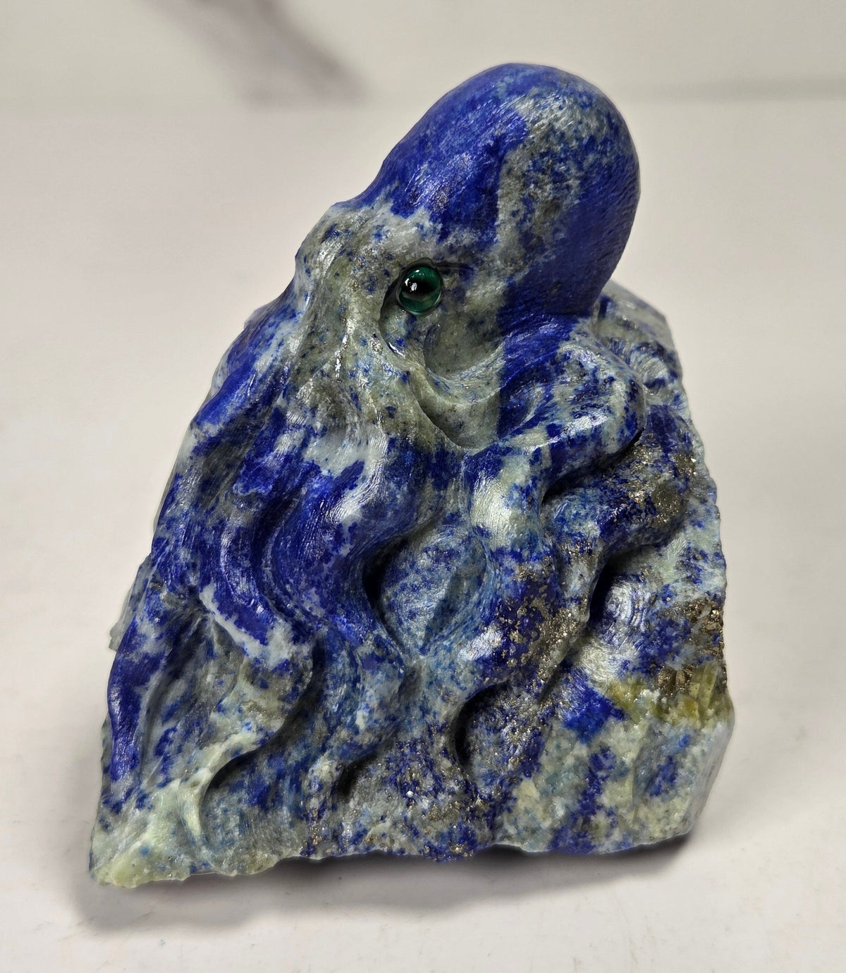 Blue crystal octopus carving with green  eyes against a marbled background