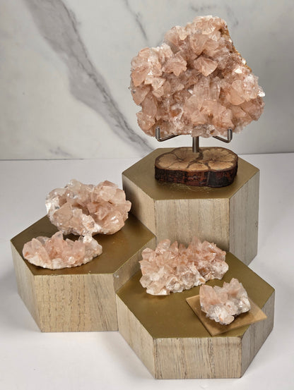 Collection of pink colored calcite specimens on a wooden stand against a marbled background