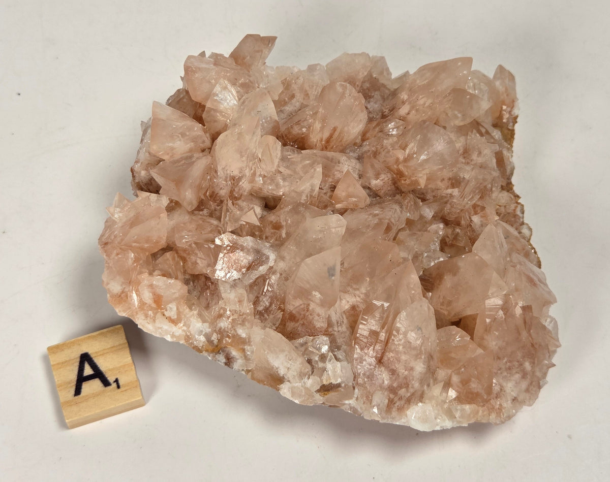 pink colored calcite specimen with a scrabble tile against a marbled background