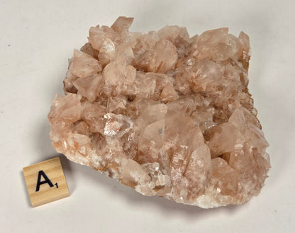 pink colored calcite specimen with a scrabble tile against a marbled background