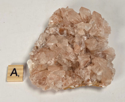 pink colored calcite specimen with a scrabble tile against a marbled background
