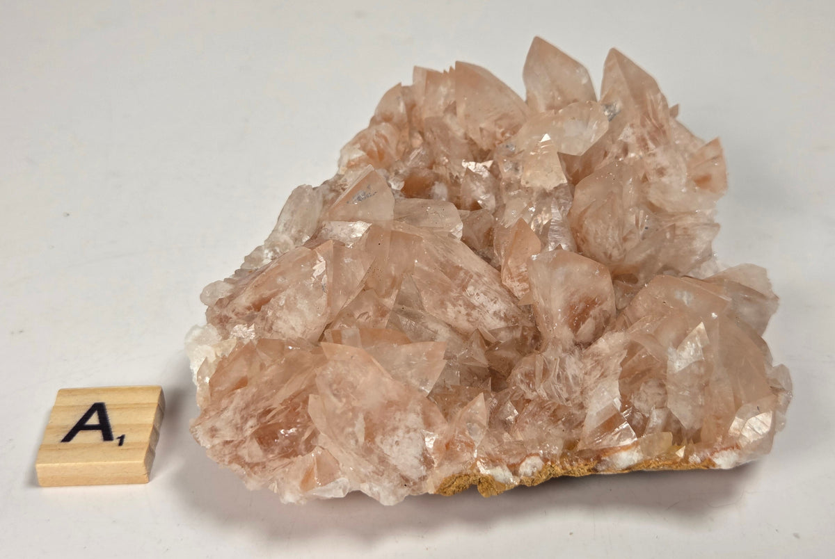 pink colored calcite specimen with a scrabble tile against a marbled background