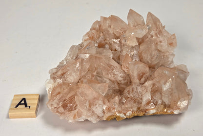 pink colored calcite specimen with a scrabble tile against a marbled background