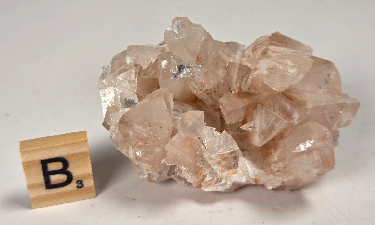 pink colored calcite specimen with a scrabble tile against a marbled background