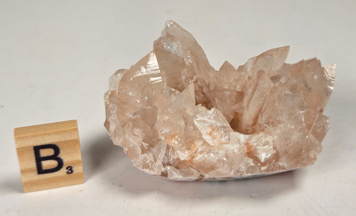 pink colored calcite specimen with a scrabble tile against a marbled background