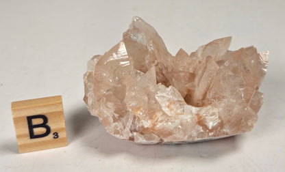 pink colored calcite specimen with a scrabble tile against a marbled background