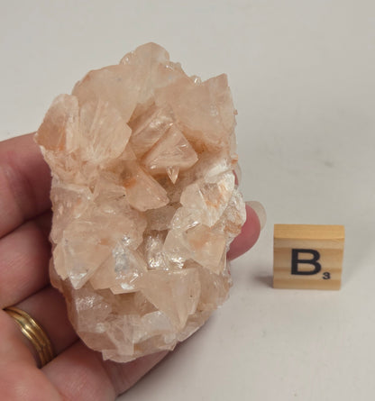 pink colored calcite specimen with a scrabble tile against a marbled background