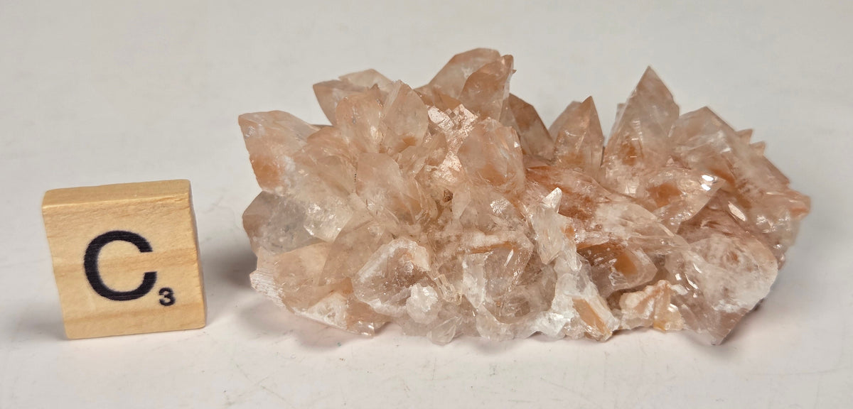 pink colored calcite specimen with a scrabble tile against a marbled background
