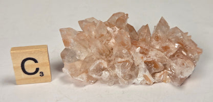 pink colored calcite specimen with a scrabble tile against a marbled background