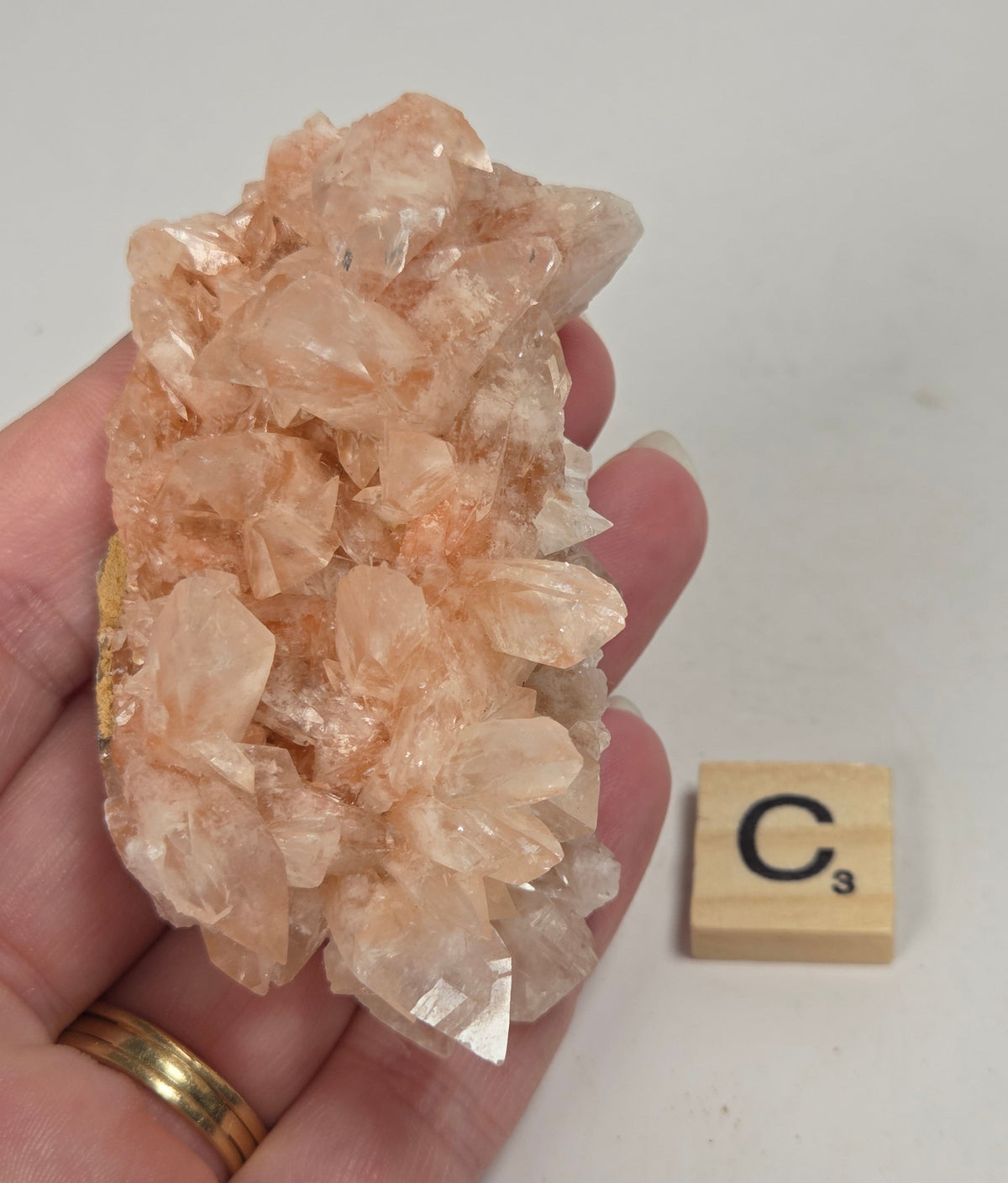 pink colored calcite specimen with a scrabble tile against a marbled background