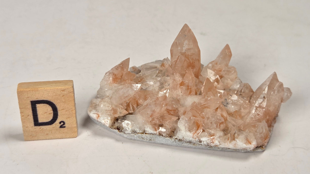 pink colored calcite specimen with a scrabble tile against a marbled background