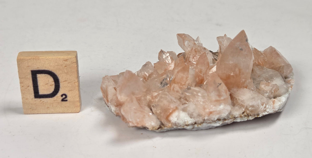 pink colored calcite specimen with a scrabble tile against a marbled background