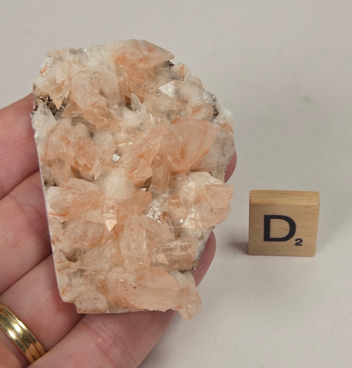 pink colored calcite specimen with a scrabble tile against a marbled background