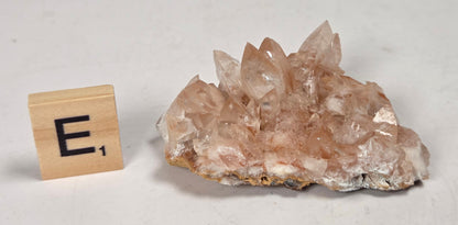 pink colored calcite specimen with a scrabble tile against a marbled background