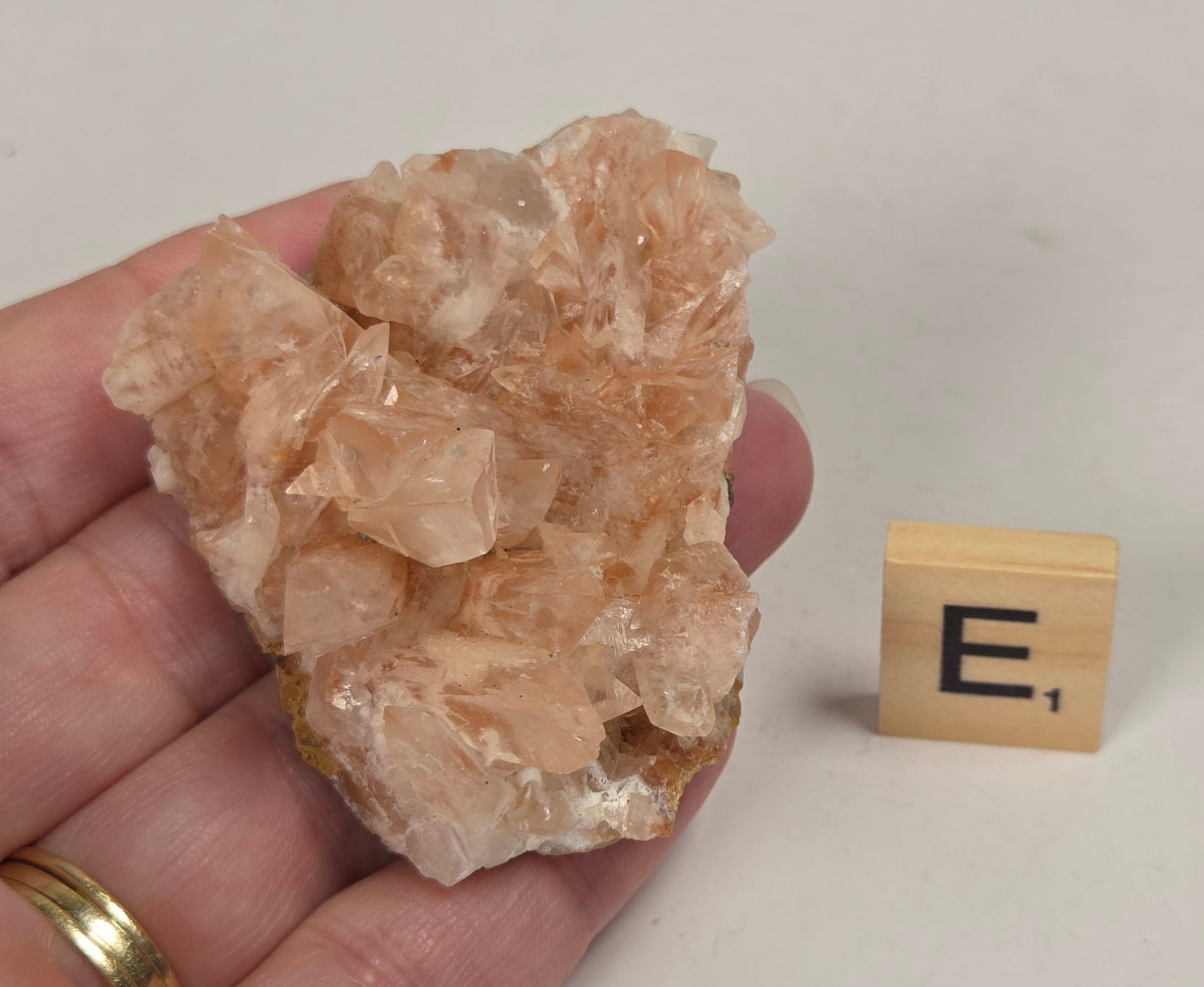 pink colored calcite specimen with a scrabble tile against a marbled background
