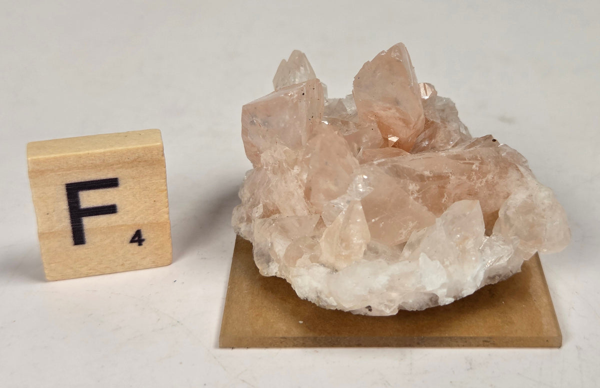 pink colored calcite specimen with a scrabble tile against a marbled background