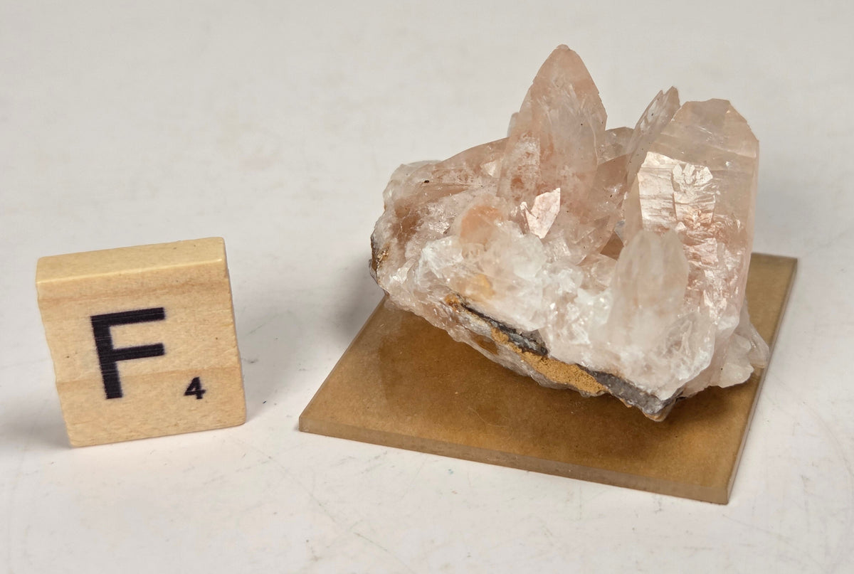 pink colored calcite specimen with a scrabble tile against a marbled background