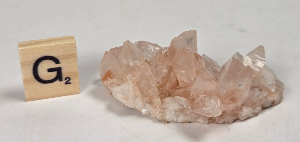pink colored calcite specimen with a scrabble tile against a marbled background