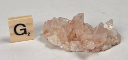 pink colored calcite specimen with a scrabble tile against a marbled background