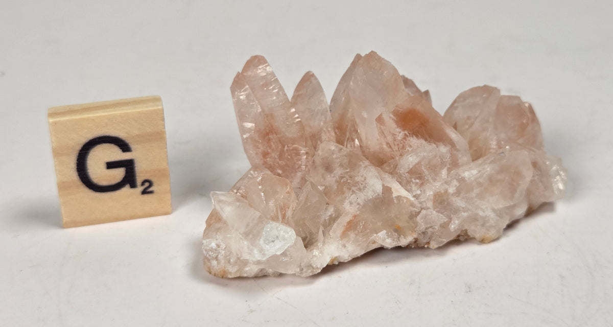 pink colored calcite specimen with a scrabble tile against a marbled background
