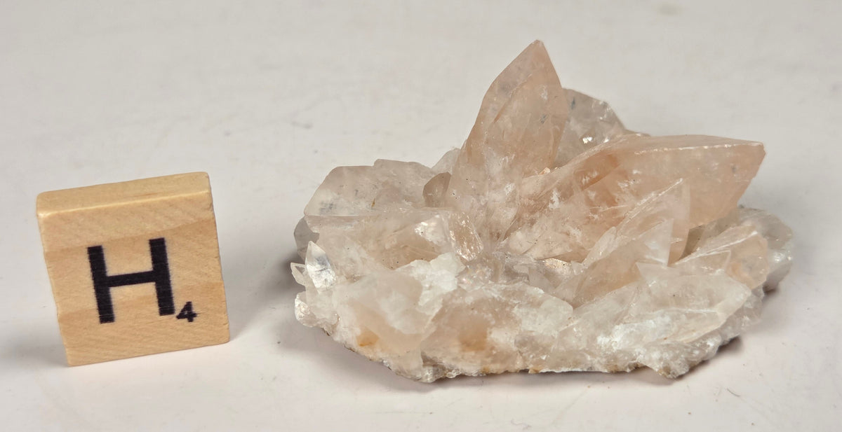 pink colored calcite specimen with a scrabble tile against a marbled background