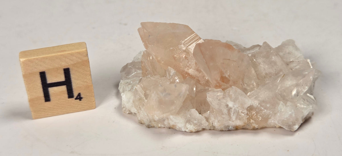 pink colored calcite specimen with a scrabble tile against a marbled background