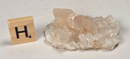pink colored calcite specimen with a scrabble tile against a marbled background