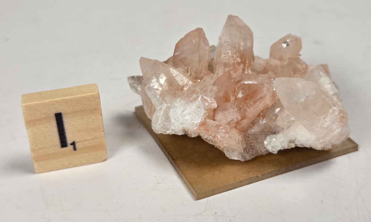 pink colored calcite specimen with a scrabble tile against a marbled background