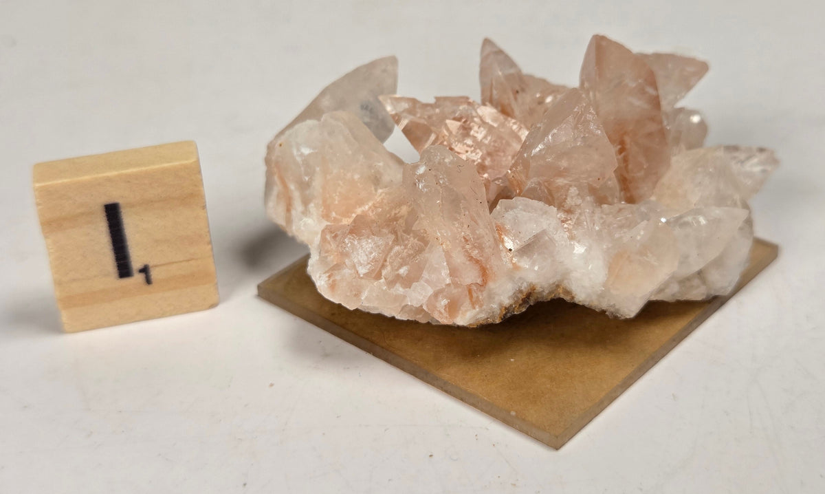 pink colored calcite specimen with a scrabble tile against a marbled background