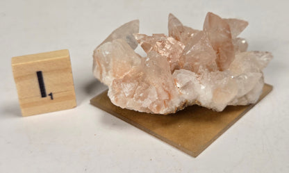 pink colored calcite specimen with a scrabble tile against a marbled background