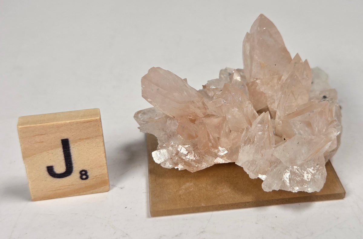 pink colored calcite specimen with a scrabble tile against a marbled background