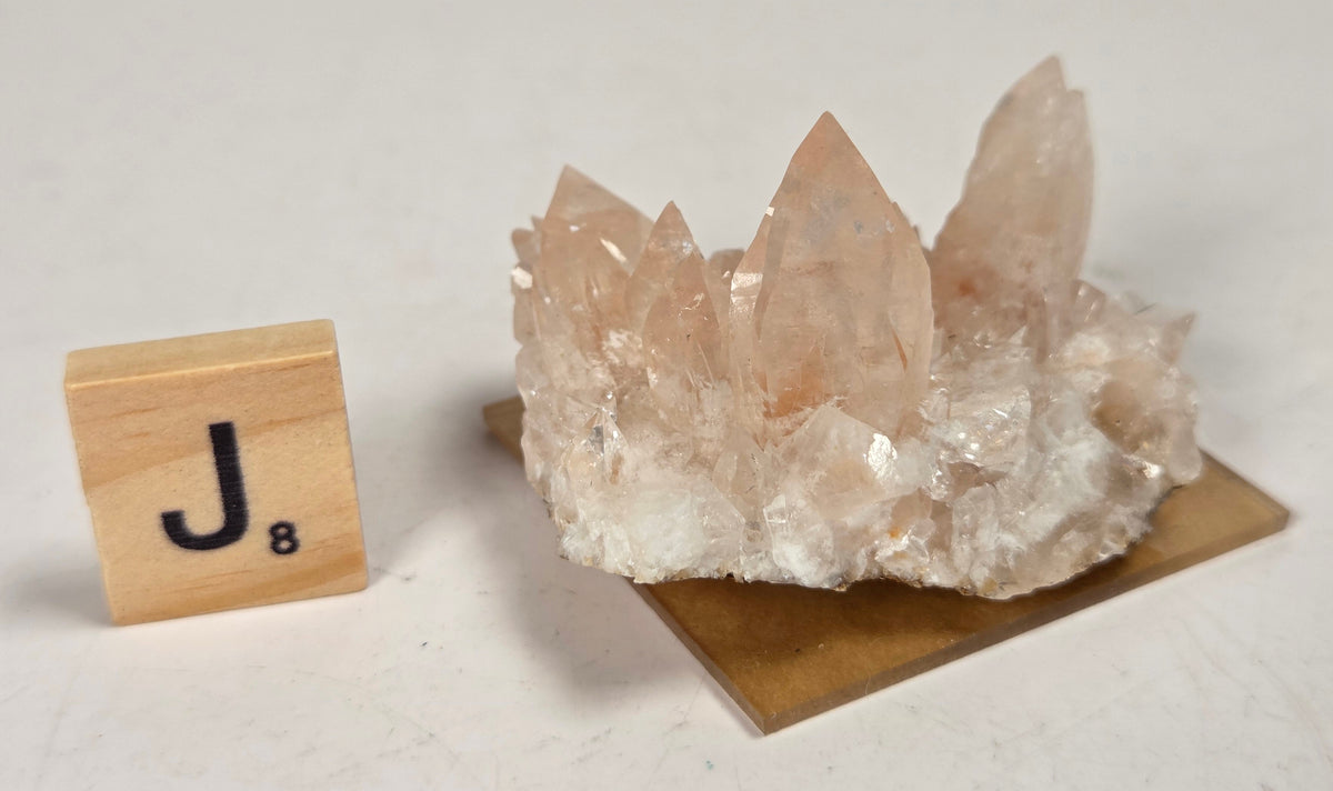 pink colored calcite specimen with a scrabble tile against a marbled background