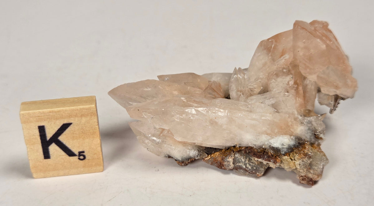 pink colored calcite specimen with a scrabble tile against a marbled background
