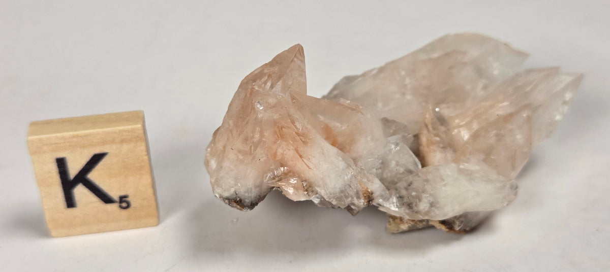 pink colored calcite specimen with a scrabble tile against a marbled background