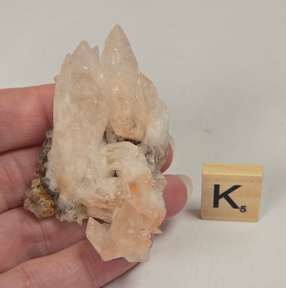 pink colored calcite specimen with a scrabble tile against a marbled background