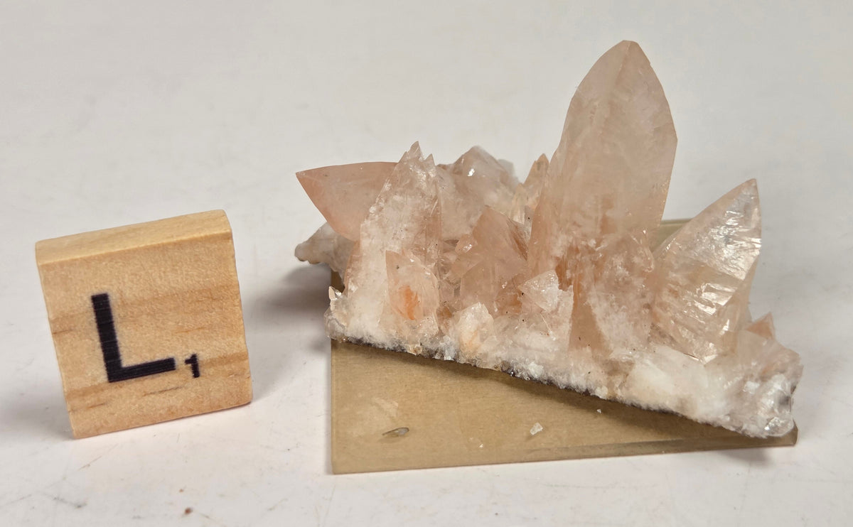 pink colored calcite specimen with a scrabble tile against a marbled background