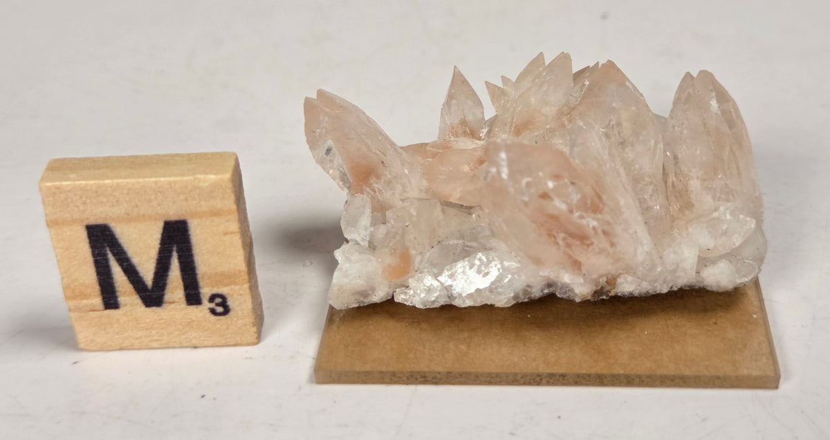 pink colored calcite specimen with a scrabble tile against a marbled background