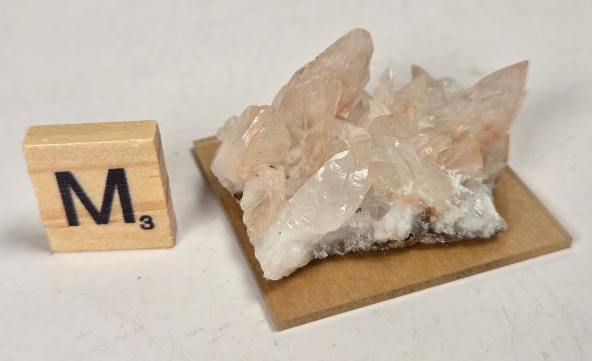 pink colored calcite specimen with a scrabble tile against a marbled background