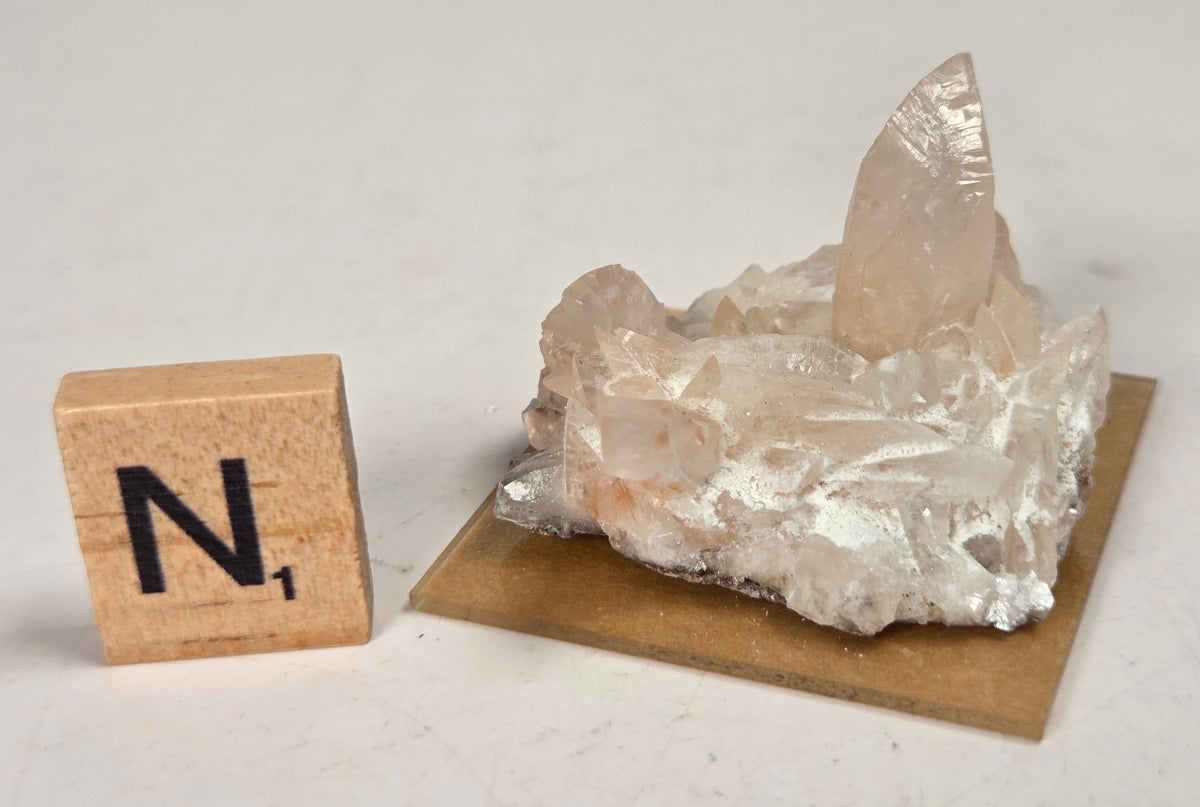 pink colored calcite specimen with a scrabble tile against a marbled background
