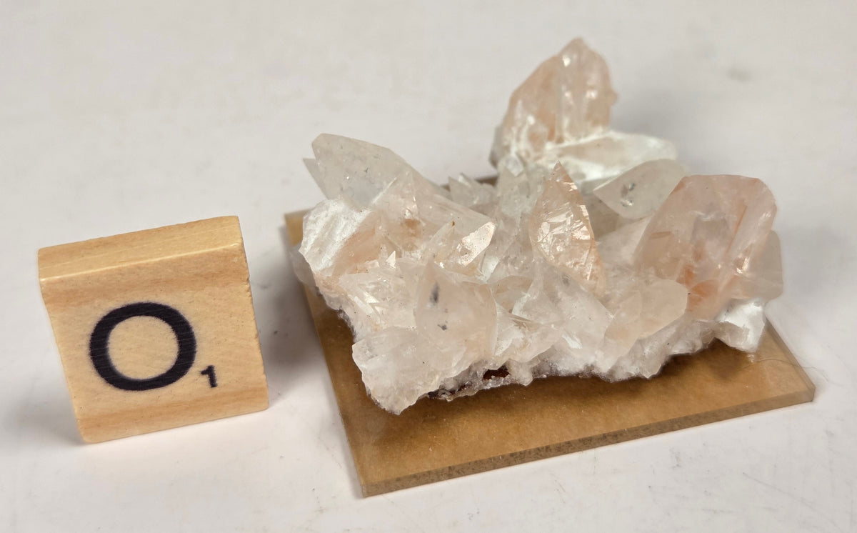 pink colored calcite specimen with a scrabble tile against a marbled background