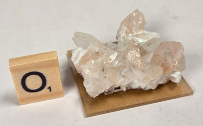 pink colored calcite specimen with a scrabble tile against a marbled background