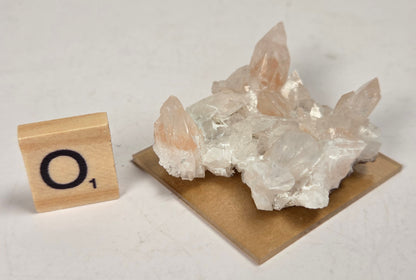 pink colored calcite specimen with a scrabble tile against a marbled background
