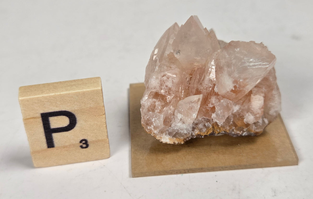 pink colored calcite specimen with a scrabble tile against a marbled background